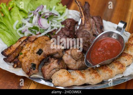 Verschiedene köstliche gegrillte Fleisch mit Salat und Zwiebeln. Gemischtes Grillfleisch mit Tomatensauce.Lamm, Huhn. Draufsicht, Nahaufnahme mit Kopierbereich. Stockfoto