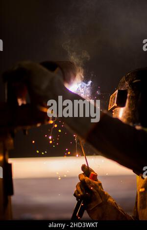 Man arbeitet am Metallschweißen von Stahl mit einem elektrischen Schweißgerät. Stockfoto