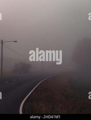Kurvige Straße mit sehr dichtem Nebel. Autoscheinwerfer, die durch Nebel ihren Höhepunkt erreichen. Kinosound. Herbstzeit. Stockfoto