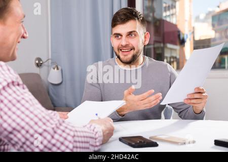 Glücklicher Mann, der mit einem männlichen Kollegen über Papiere sprach Stockfoto