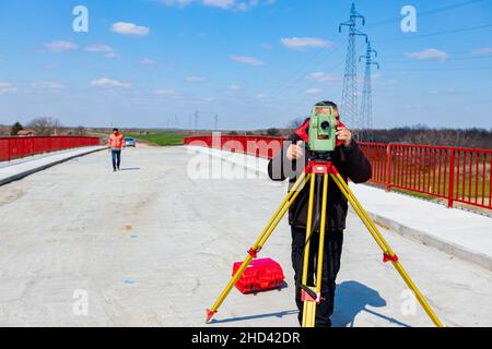 Vermessungsingenieur misst Brücke im Bau, Baustelle. Vermesser sorgen für präzise Messungen, bevor sie große Bauprojekte durchführen. Stockfoto