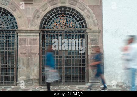 Die Leute gehen tagsüber schnell auf der Straße vor einer gewölbten Steintür mit einem Metallzaun Stockfoto