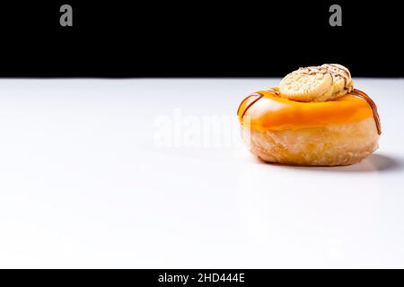 Nahaufnahme eines mit Schokolade und Keksen bemalten cremefarbenen Donuts auf einem weißen Tisch und schwarzem Hintergrund.das Foto wurde im horizontalen Format und aufgenommen Stockfoto