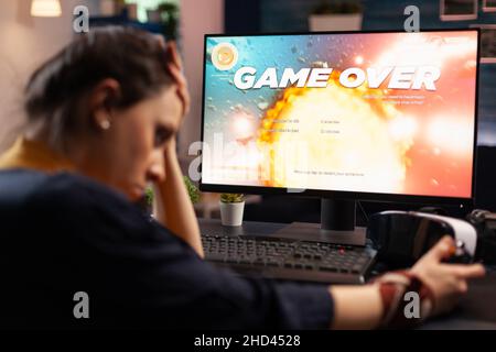 Frustrierte Frau verliert Online-Videospiele auf dem Computer. Enttäuschte Person, die auf dem Monitor spielt, den Controller verwendet und sich über das verlorene Spiel traurig fühlt. Gamer mit elektronischem E-Sport. Stockfoto