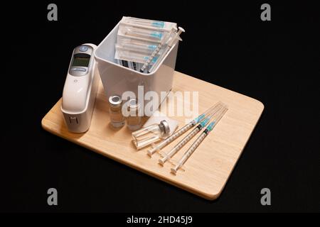 Medizinische Geräte, einschließlich Spritzen mit hypodermischen Nadeln mit Sicherheitsverschlüssen, Ohrtemperaturmonitor und Fläschchen mit einer klaren Flüssigkeit. Stockfoto