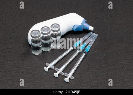 Medizinische Geräte, einschließlich Ohrthermometer, Spritzen mit hypodermischen Nadeln mit Sicherheitsverschlüssen und Fläschchen mit einer klaren Flüssigkeit. Stockfoto