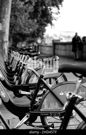 Vertikale Aufnahme einer Reihe von Leihfahrrädern, die in der Nähe des Bürgersteiges geparkt sind, Graustufen Stockfoto