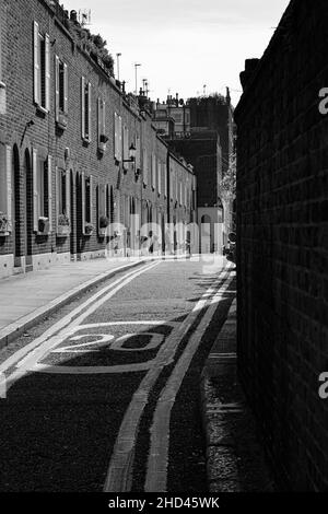 Vertikale Aufnahme einer engen Straße, umgeben von Hausgebäuden, Graustufenbild, London Stockfoto