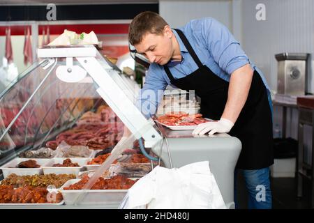 Lächelnd Metzger in Metzgerei mit Schale mit frischen rohen Fleisch steak Schnitzel Stockfoto