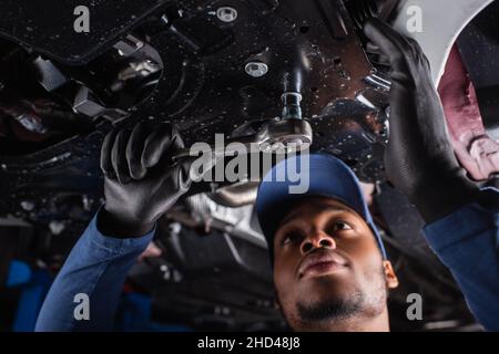 Low-Angle-Ansicht des afroamerikanischen Mechanikers in Kappe mit Schraubenschlüssel während der Arbeit im Autodienst Stockfoto