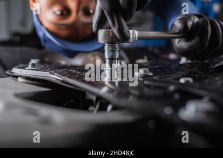 Beschnittene Ansicht eines afroamerikanischen Arbeiters, der einen Schraubenschlüssel auf dem Auto in der Garage verwendet Stockfoto