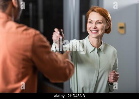 Zufrieden mit dem Autohändler, der dem unscharfen afroamerikanischen Kunden den Schlüssel gibt Stockfoto