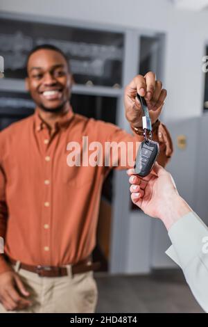 Verschwommenes lächeln des afroamerikanischen Autohändlers beim Geben des Schlüssels an den Kunden Stockfoto
