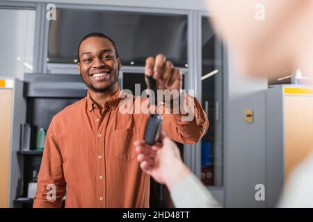 Zufrieden african american Autohändler geben Schlüssel zu verschwommenen Kunden Stockfoto
