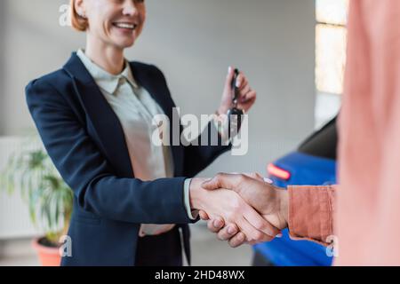 Teilansicht des Autohändlers, der den Schlüssel hält, während er mit einem unscharfen afroamerikanischen Kunden die Hände schüttelt Stockfoto