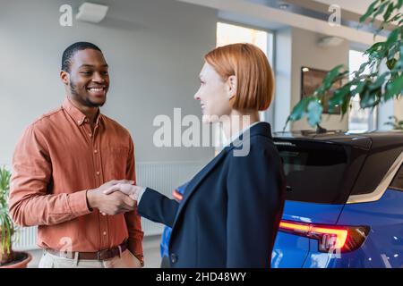 Glücklicher afroamerikanischer Mann und Autohändler, der sich in der Nähe des Autos die Hände schüttelte Stockfoto