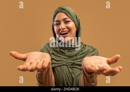 Viel Spaß. Aufgeregte arabische Frau im Hijab, die die Hände auf die Kamera streut und emotional auf gute Nachrichten reagiert Stockfoto