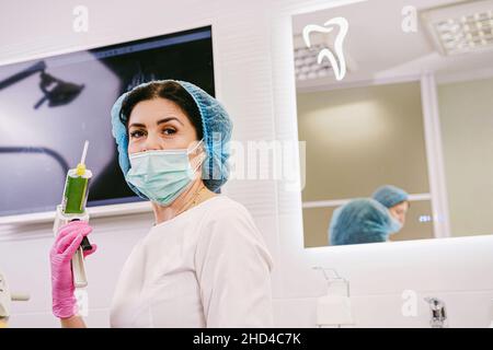 Nahaufnahme einer Zahnärztin in medizinischer Uniform, die in ihrer Hand eine Zahnfüllpistole in ihrer medizinischen Klinik hält. Stockfoto