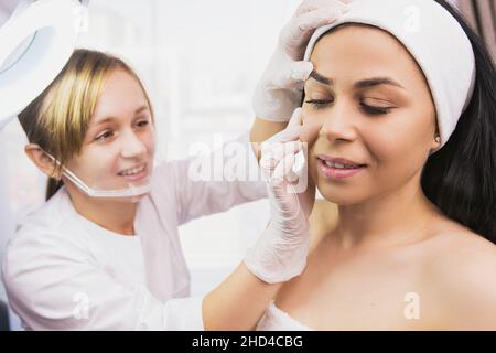Spezialkosmetologin inspiziert ihr Gesicht der Patientin in einem Kursalon der Klinik, um das erforderliche Verfahren zu wählen. Stockfoto
