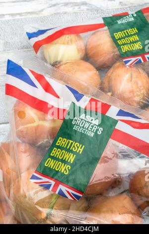 BRAUNE Zwiebeln/Allium cepa in Kunststoffpackungen. Auch gelbe Zwiebeln genannt. Für gängige Küchenzutaten, Union Jack auf Lebensmittelverpackungen Stockfoto