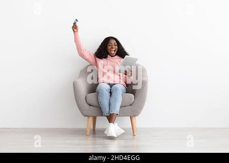 Emotionale afroamerikanische Frau mit Kreditkarte und digitalem Tablet Stockfoto