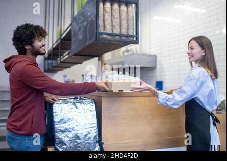 Lockiger junger Courier, der die Essensbox zur Lieferung nimmt Stockfoto