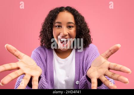 Emotionale junge afroamerikanische Frau, die die Hände vor die Kamera streicht, OMG schreit und auf rosa Hintergrund einen großen Sieg feiert Stockfoto