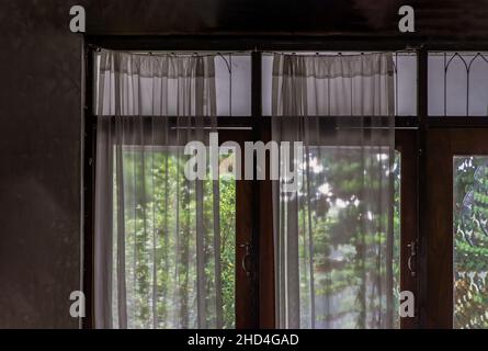 Einfaches Glas aus Holz und weiße Spitzenvorhänge mit Sonnenlicht, das im traditionellen thai-Haus durchscheint, Architektur im Thai-Stil, kein Fokus, Stockfoto