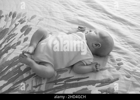 Neugeborenes Mädchen liegt auf dem Bett. Das Baby ist gerade zwei Wochen alt geworden. Pflegekonzept für Neugeborene. Stockfoto