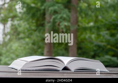 Offenes Buch auf dem Garten Holztisch, grüner Hintergrund, Kopierraum Stockfoto