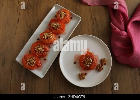 Quitte-Dessert, im Ofen gebackene Quitte in dickem Sirup. Weiße Platte und Holzhintergrund. Konzept und Idee für die Präsentation von Lebensmitteln. Traditionelle türkische Küche. Stockfoto