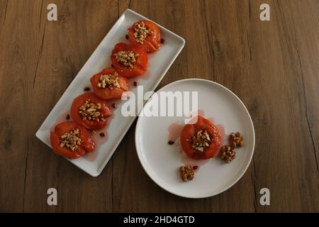 Quitte-Dessert, im Ofen gebackene Quitte in dickem Sirup. Weiße Platte und Holzhintergrund. Konzept und Idee für die Präsentation von Lebensmitteln. Traditionelle türkische Küche. Stockfoto