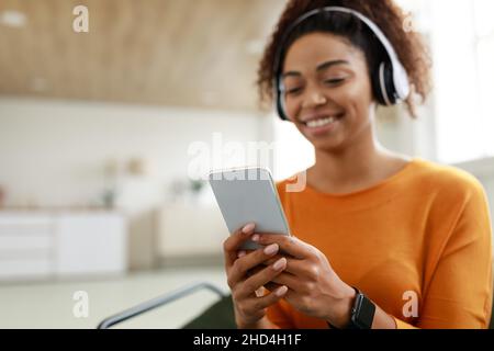 Lächelnde schwarze Frau mit schnurlosem Kopf und Mobiltelefon Stockfoto