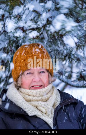 Frau mittleren Alters im Winter mit schneebedeckter Kiefer im Freien Stockfoto