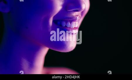 Nahaufnahme des Lächelns einer jungen Frau, beleuchtet mit buntem Neonlicht Stockfoto