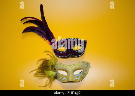 Zwei Karnevalsmasken, eine gelbe und eine violette Federwithe auf gelbem Grund Stockfoto