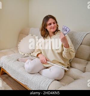 Musikerin mit Geld in US-Dollar zu Hause auf dem Sofa im Wohnzimmer Stockfoto