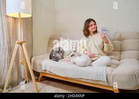 Musikerin mit Geld in US-Dollar zu Hause auf dem Sofa im Wohnzimmer Stockfoto