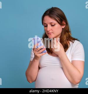 Mobiltelefon in den Händen einer Schwangeren, Studio auf blauem Hintergrund Stockfoto