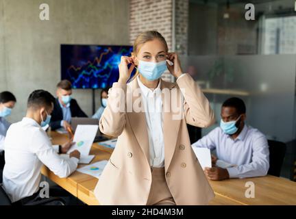 Geschäftsfrau, Die Vor Dem Treffen Mit Kollegen Im Büro Eine Medizinische Gesichtsmaske Aufsetzt Stockfoto