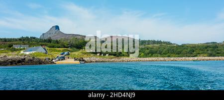 Isle of Eigg im Sommer. Ein Panoramablick auf die Insel Eigg vom Meer aus, mit Teeshop, Pier, Campingplätzen und der Dominante einer SGU Stockfoto