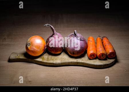 Rohes Gemüse für die Suppe auf dem hölzernen Schneidebrett - Zwiebeln, Rüben, Karotten. Das Konzept der Vegetarismus und gesunde Ernährung. Stockfoto