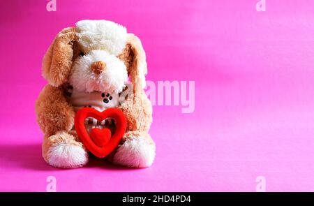 Weiße und braune Hundepuppe mit rotem Herz auf rosa Hintergrund.ein Symbol der Liebe. Valentinstag Stockfoto