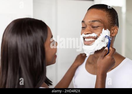 Fürsorgliche Junge Schwarze Frau Hilft Ihrem Freund Mit Rasier Gesicht Stockfoto