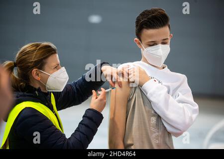 Stuttgart, Deutschland. 03rd Januar 2022. Ein Malteser-Mitarbeiter impft in einer Halle der Messe Stuttgart ein Kind gegen den Corona-Virus. Unter dem Motto "Wir impfen DAS LAND - Teil II" findet vom 03. Bis 06. Januar 2022 in der Messe Stuttgart eine Drive-in-Impfkampagne statt, bei der Interessierte, darunter auch Kinder, von 7 bis 11 Uhr in der Messehalle 9 geimpft werden können. Quelle: Christoph Schmidt/dpa/Alamy Live News Stockfoto