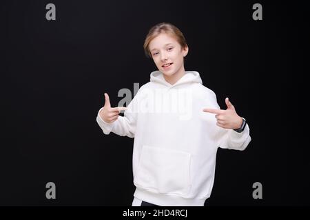 Niedliches Portrait hübscher junger Mann in weißem, blanken Kapuzenpullover oder Sweatshirt mit Platz für dein Logo oder Design auf schwarzem Hintergrund. Modell zum Drucken Stockfoto