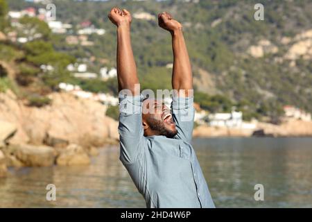 Aufgeregt Mann mit schwarzer Haut feiert Erfolg heben die Arme am Strand Stockfoto