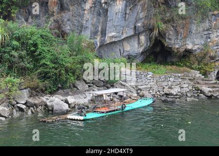 Traditionelles Bambusboot auf dem Fluss Li in Yangshuo China. Grauer Karst (Kalkstein) Berg im Hintergrund mit Bäumen und grünem Boot. Stockfoto