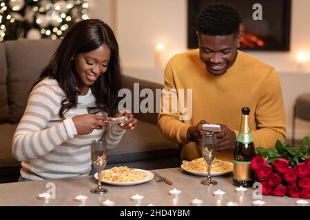 Happy Black Paar mit Smartphones feiern Valentinstag zu Hause Stockfoto