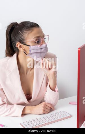 Salisbury, Wiltshire, Großbritannien. 2021. Attraktive Frau trägt rosa Gesichtsmask und mit einem Computer und Tastatur. Stockfoto